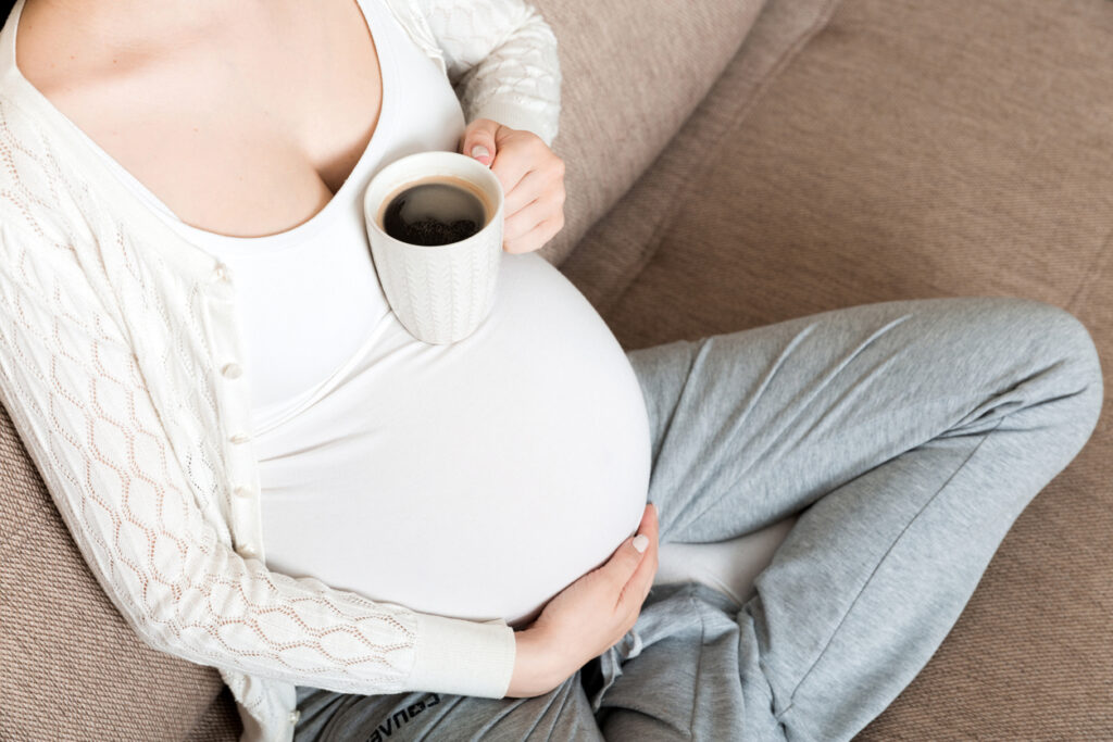 chica embarazada sentada en el sofá con café Taza de café en la mano. mañana de maternidad.