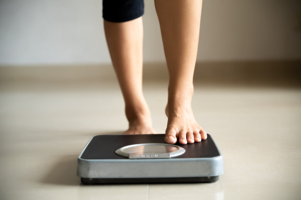 Mujer subiendo a una báscula de peso en casa. Estilo de vida saludable, alimentación y concepto deportivo.