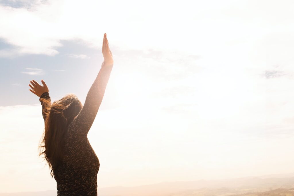 mujer 45 años levanta los brazos como gesto de felicidad en un paisaje idílico de puesta de sol.