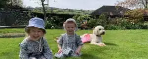 Two young toddlers smiling on grass with a dog