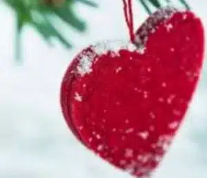 Red heart ornament handing on snowy christmas tree