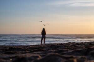Woman on beach looking out to sea and some sea gulls