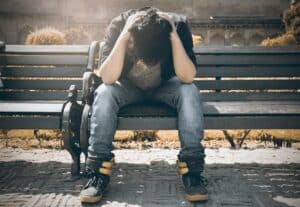 Man on bench with heads in his hands, maybe because he's wearing rubbish trainers